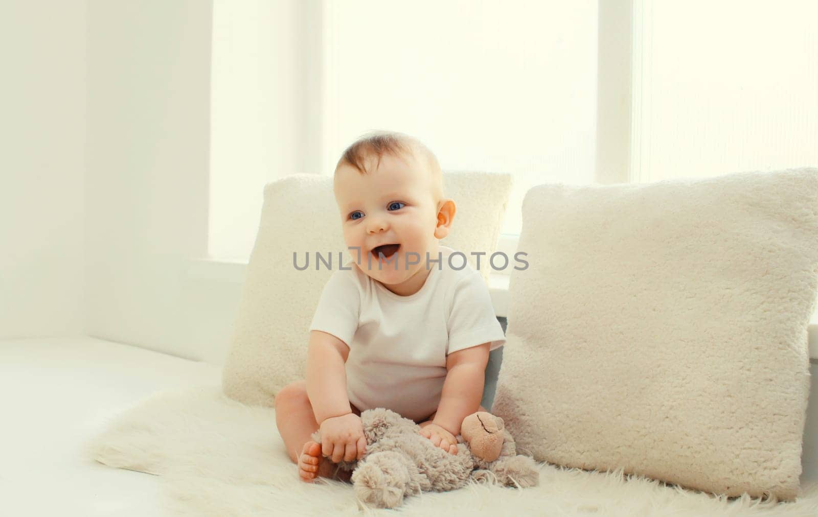 Happy cute little baby playing with teddy bear toy on the floor in white room at home