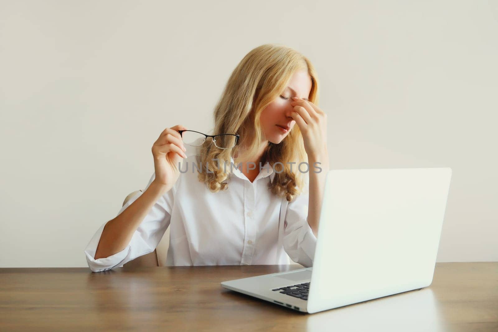 Tired overworked woman employee suffering from headache, rubbing her dry eyes, working with laptop sitting at desk in office
