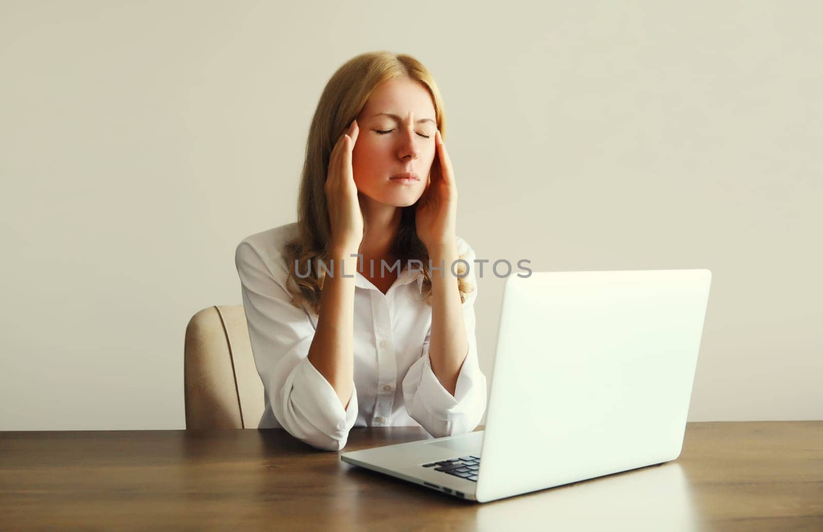 Tired overworked woman employee suffering from headache, migraine, working with laptop sitting at desk in office in morning