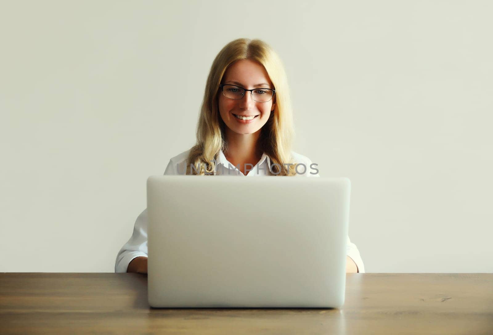 Happy young woman working with laptop sitting at desk in office or home