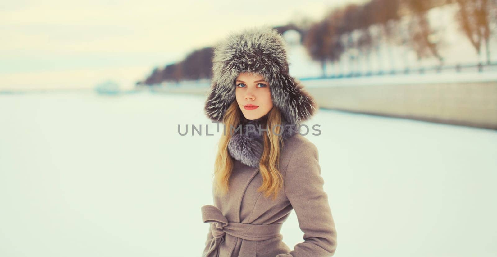 Portrait of beautiful blonde young woman posing in winter hat outdoors in park