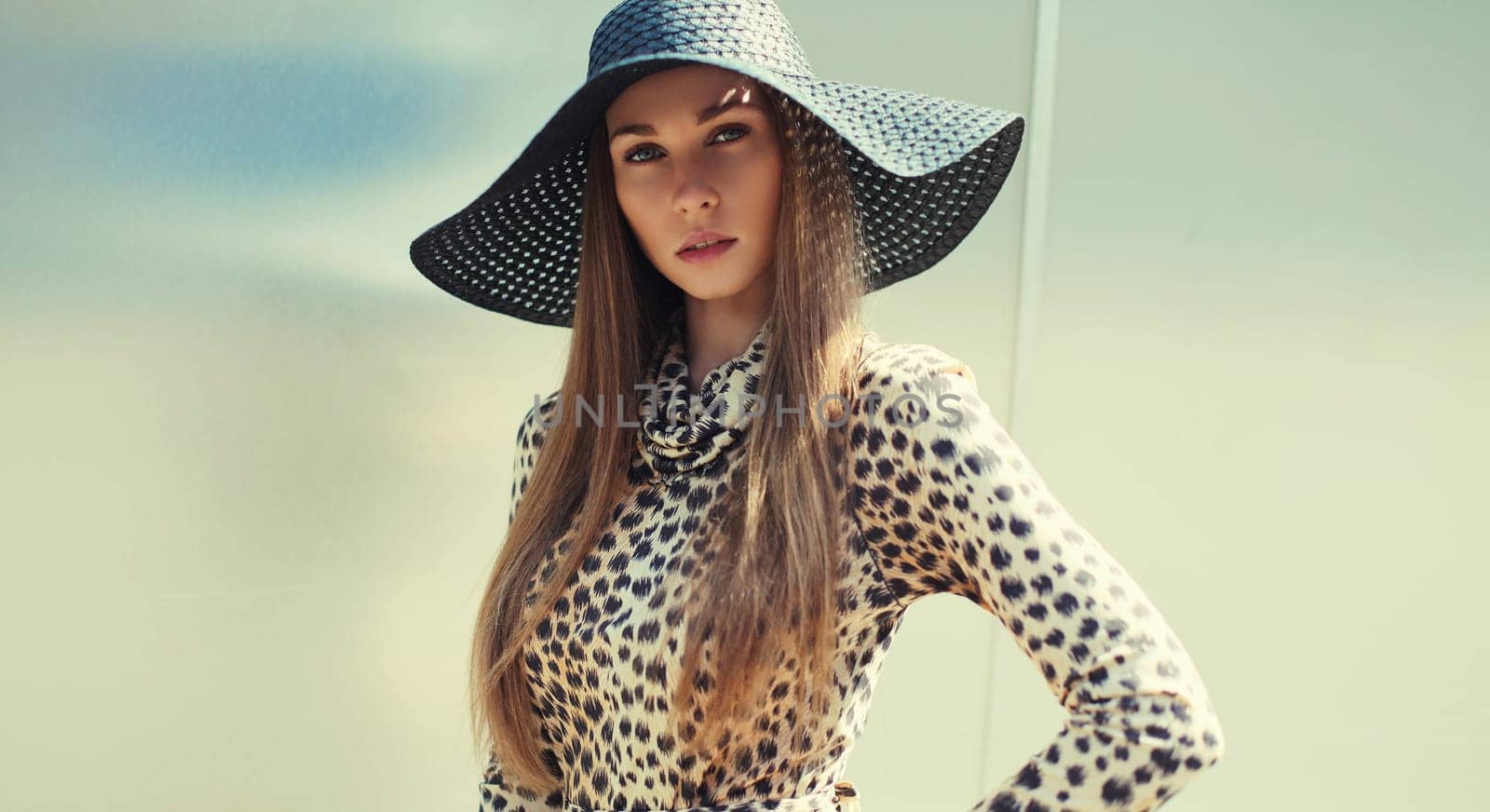 Portrait of beautiful blonde young woman wearing summer straw hat, leopard dress in the city