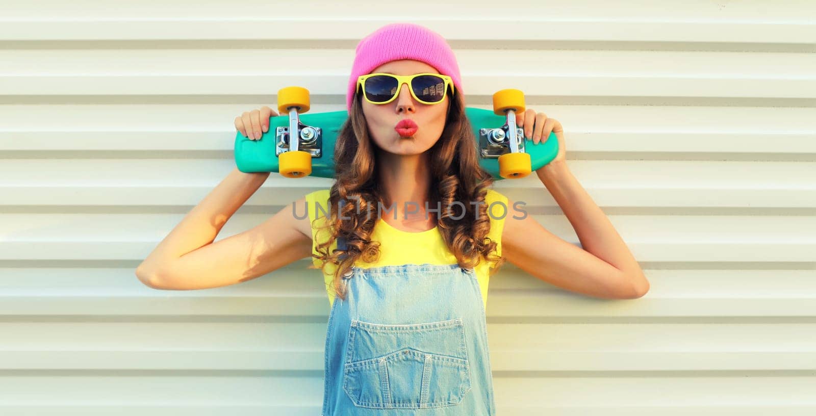 Summer portrait of happy cheerful young woman posing with skateboard in colorful clothes on white background