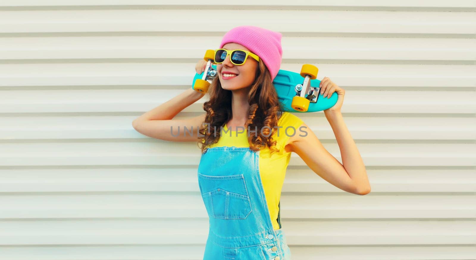 Summer portrait of happy cheerful smiling young woman with skateboard in colorful clothes on white background