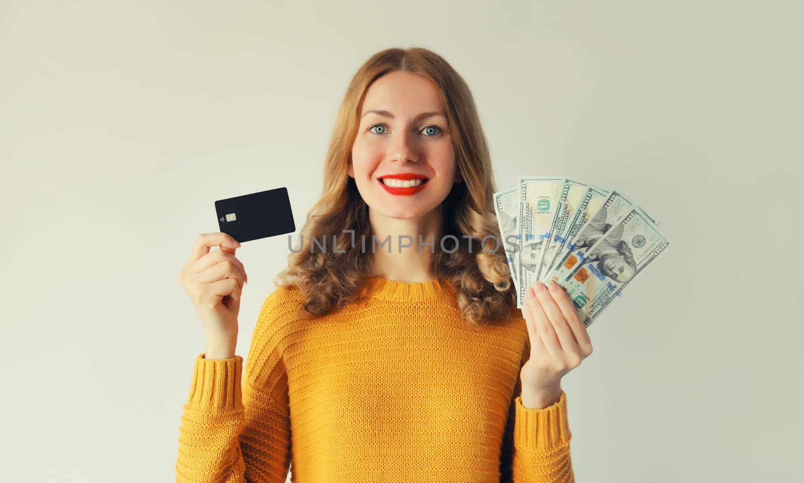 Portrait of happy smiling young woman holding plastic credit bank card and cash money in dollar bills