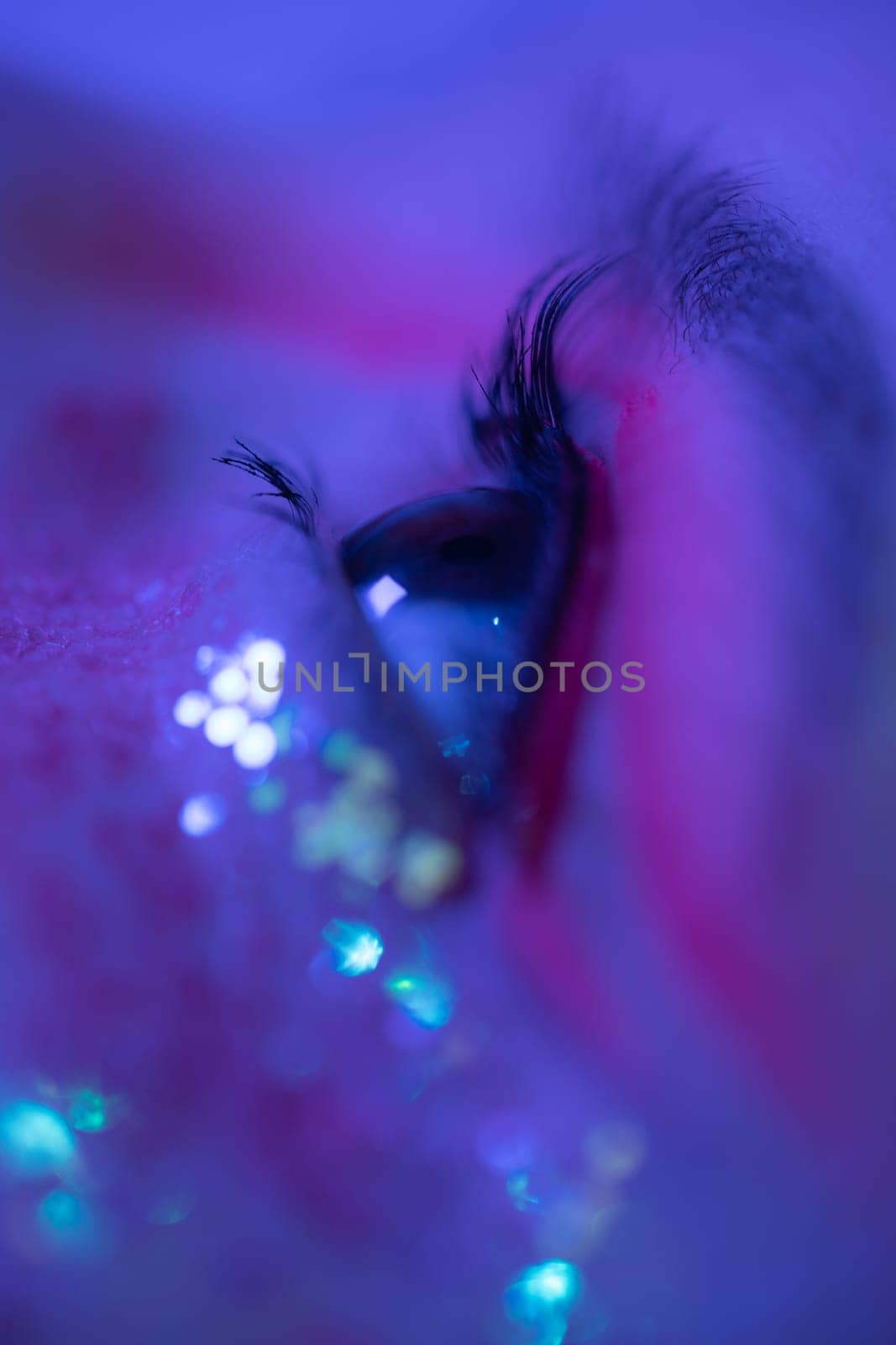 Extreme closeup view of female eye with shiny make-up with sequins and arrows. Cinematic macro shot of female eye illuminated pink-blue color neon light. Selective focus, side view. Part of series