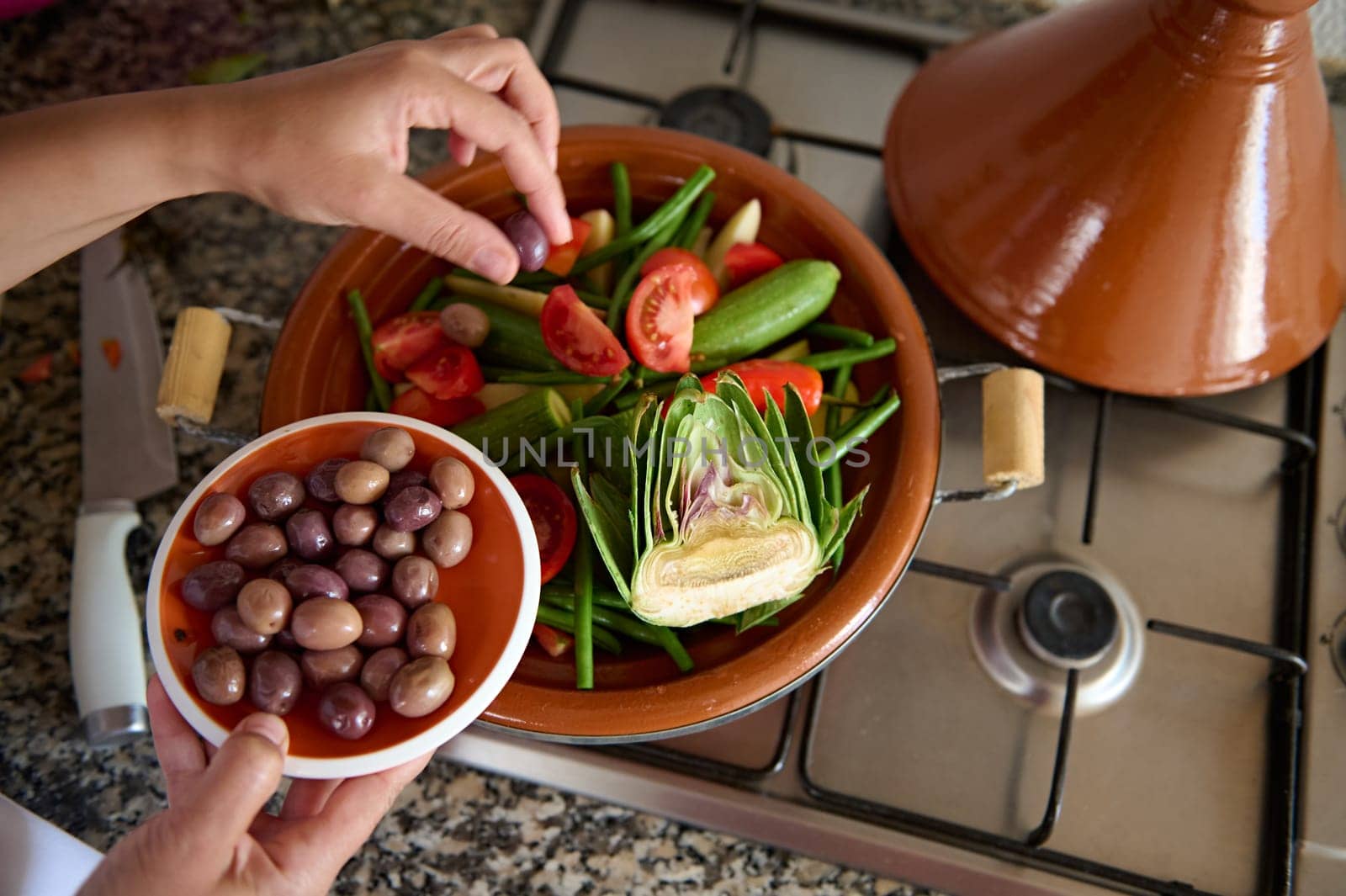 View from above of housewife adding olives into a meal while cooking healthy vegetarian meal in tagine. The concept of traditional Moroccan cuisine