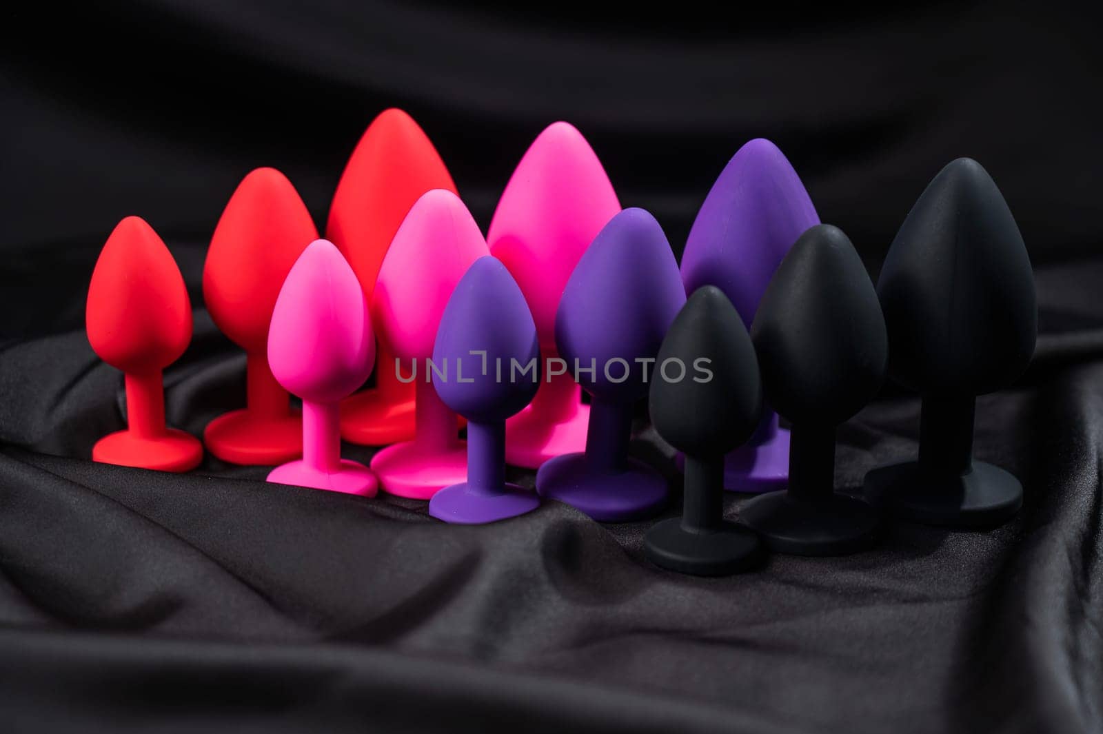 A set of silicone anal plugs in different colors and sizes on a black silk sheet