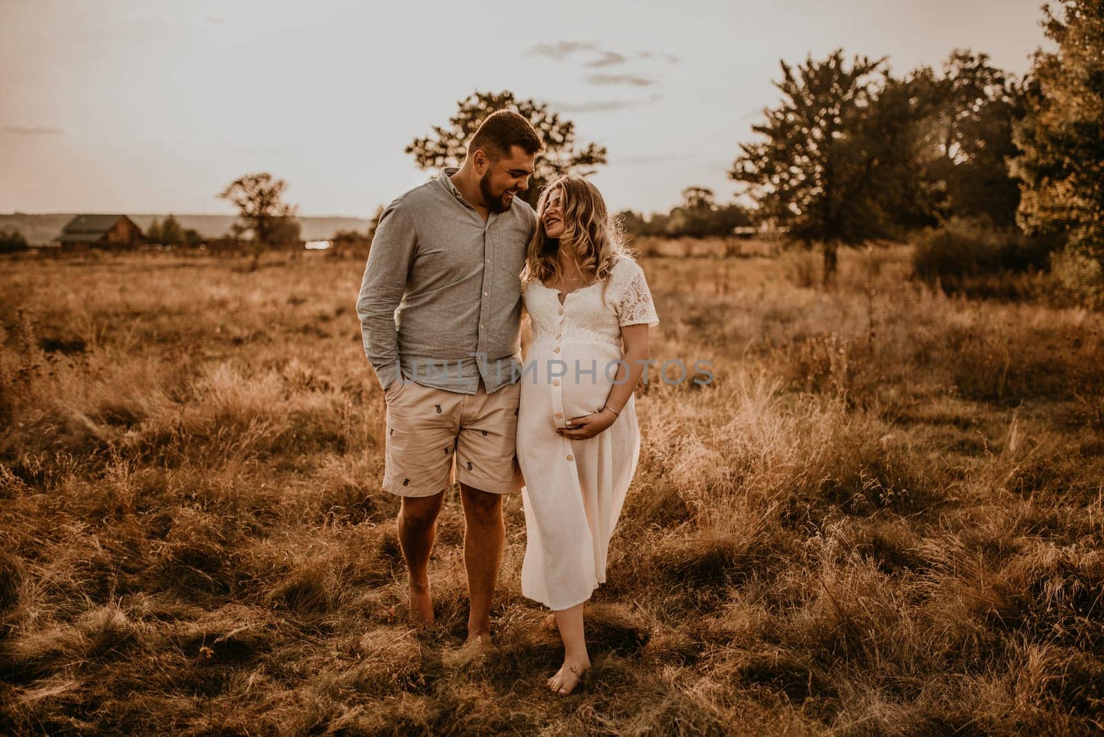 Happy family pregnant caucasian blonde woman walks with husband in meadow in summer. by AndriiDrachuk