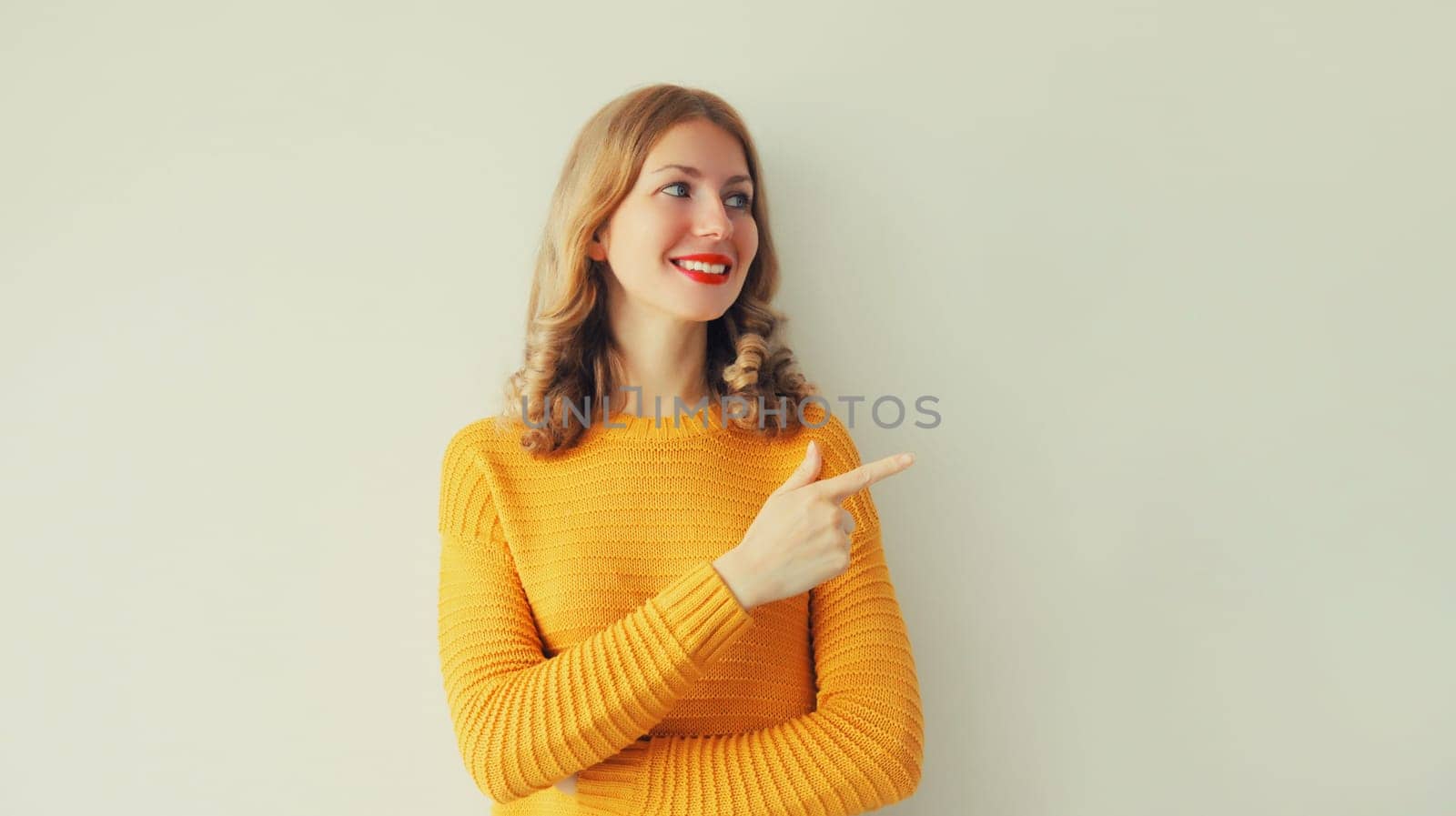 Portrait of happy smiling young woman pointing her finger to the side and looking away on studio background, blank copy space for advertising text