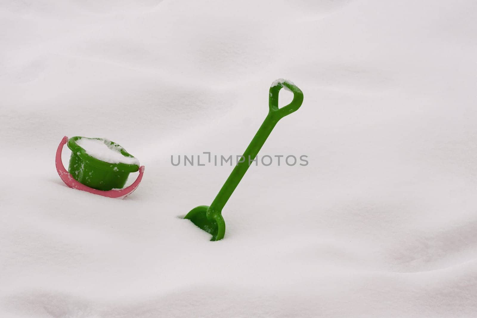 Children's green shovel and bucket of snow on a snowy surface. Winter active recreation, accessories for children's educational games.