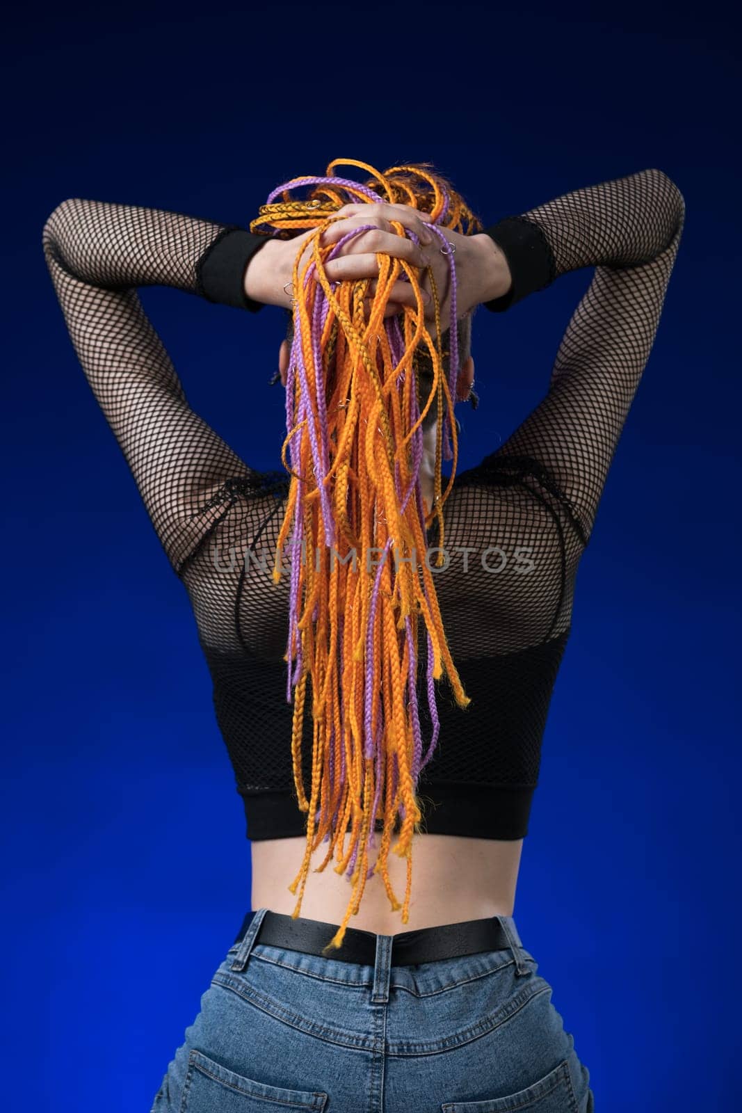 Rear view of unrecognizable woman with orange color without dangerous dreadlocks hairstyle. Studio shot on blue background. Part of photo series