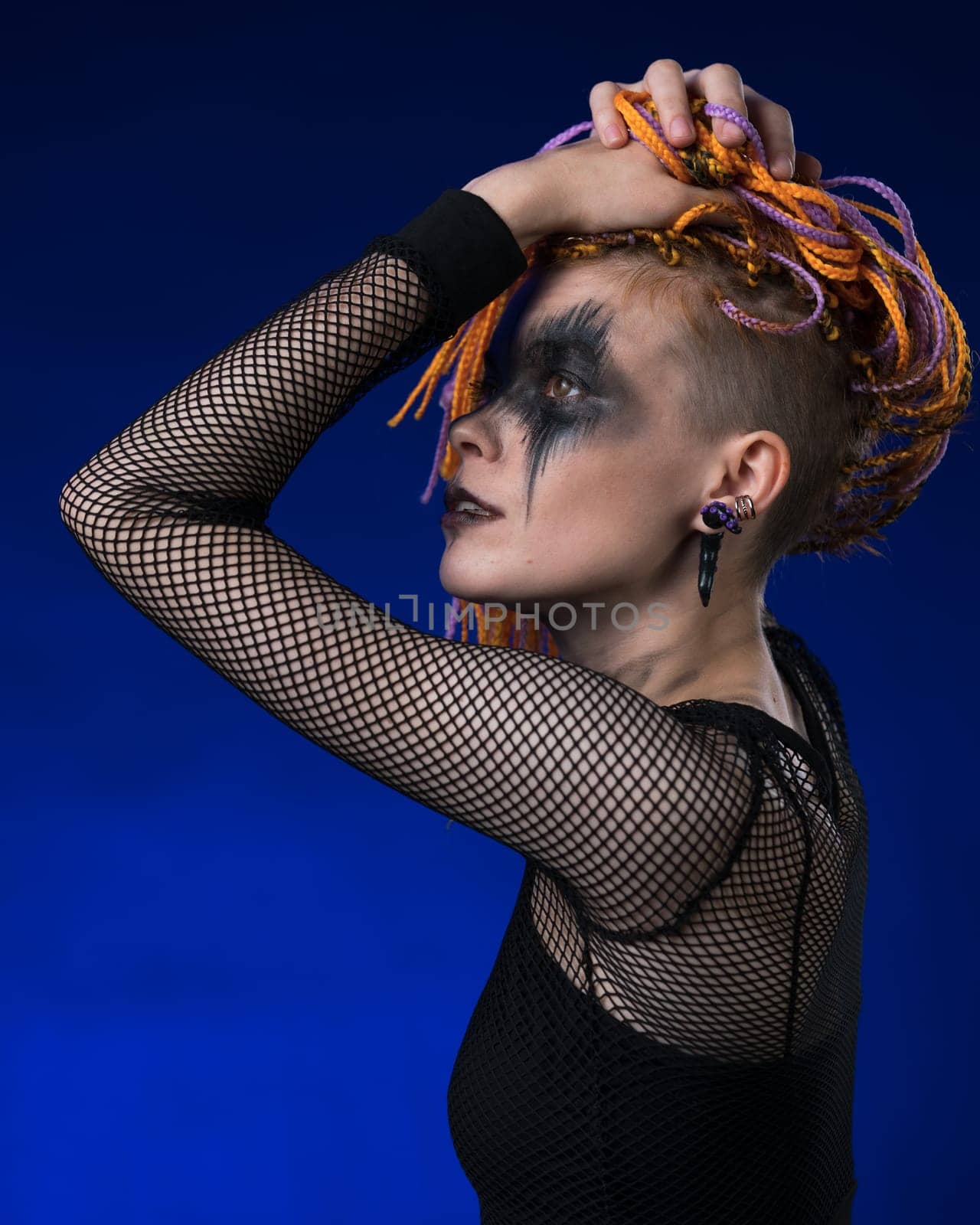 Cinematic portrait of beauty woman with colored braids hairdo and spooky stage make-up painted on face. Studio shot dramatic portrait on blue background. Part of photo series