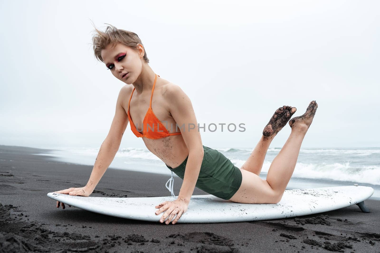 Sports fashion model surfer lying on front on surfboard, leaning on hands, arching back and looking at camera. Sexuality sportswoman warm up exercise before training during summer beach holidays