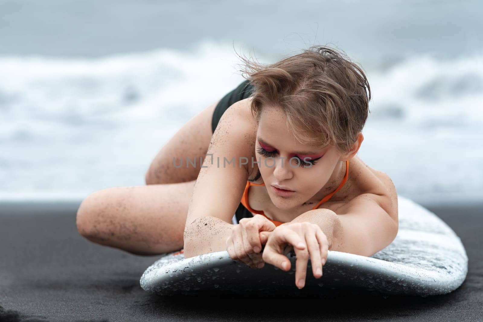 Close-up view of woman surfer lying on surfboard with eyes closed, looks so relaxed and peaceful. Amazing blonde sports fashion model with bright makeup enjoying moment during summer beach holiday