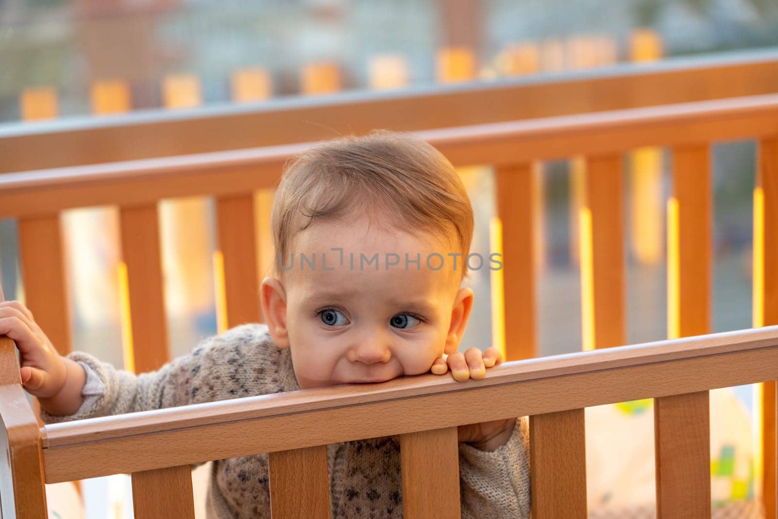 baby sadly bites the edge of the crib with his teeth while waiting for his parents.