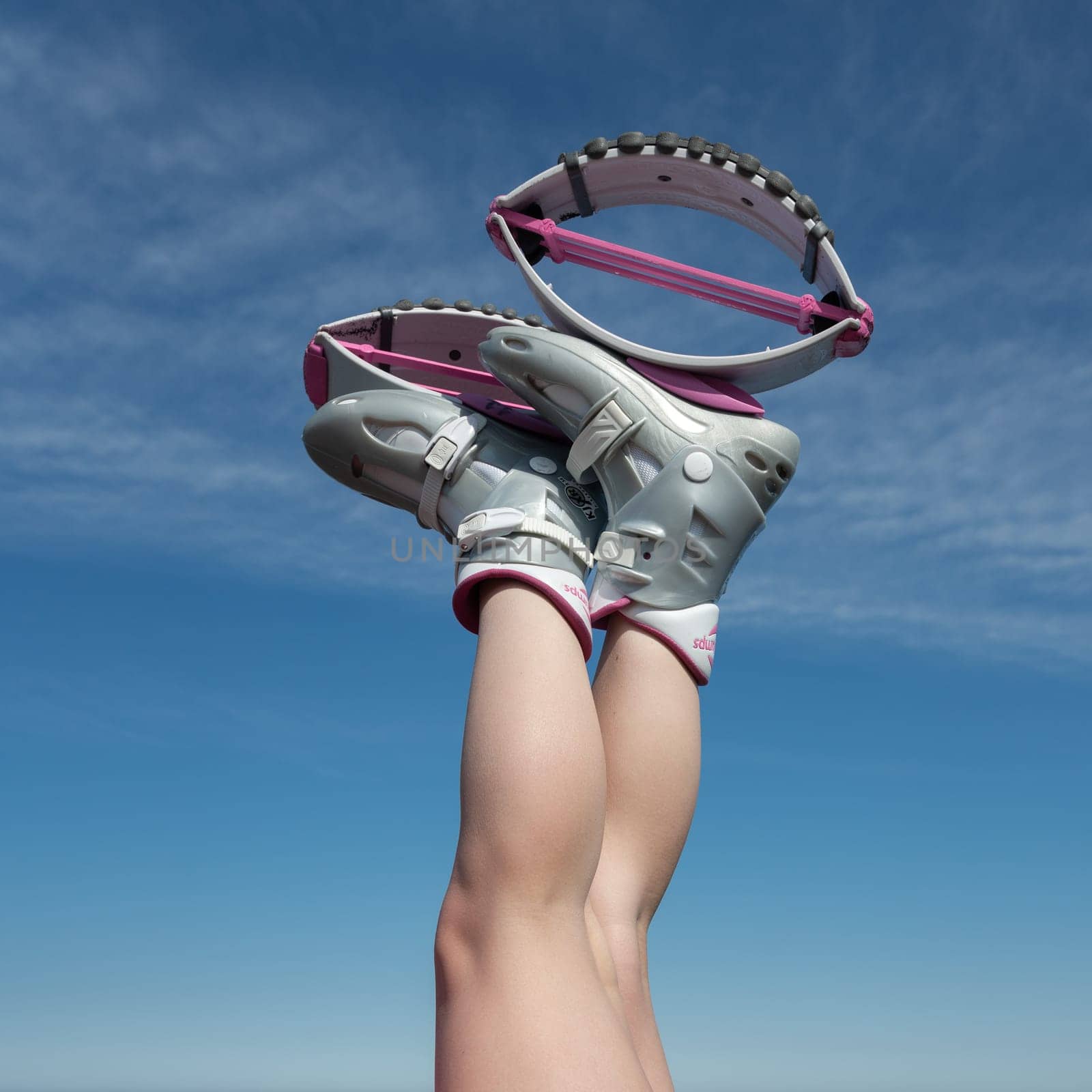 Close-up woman crossed legs up in air shod in sports Kangoo Jumps boots during aerobic exercising outdoors on background of blue sky on sunny summer day by Alexander-Piragis