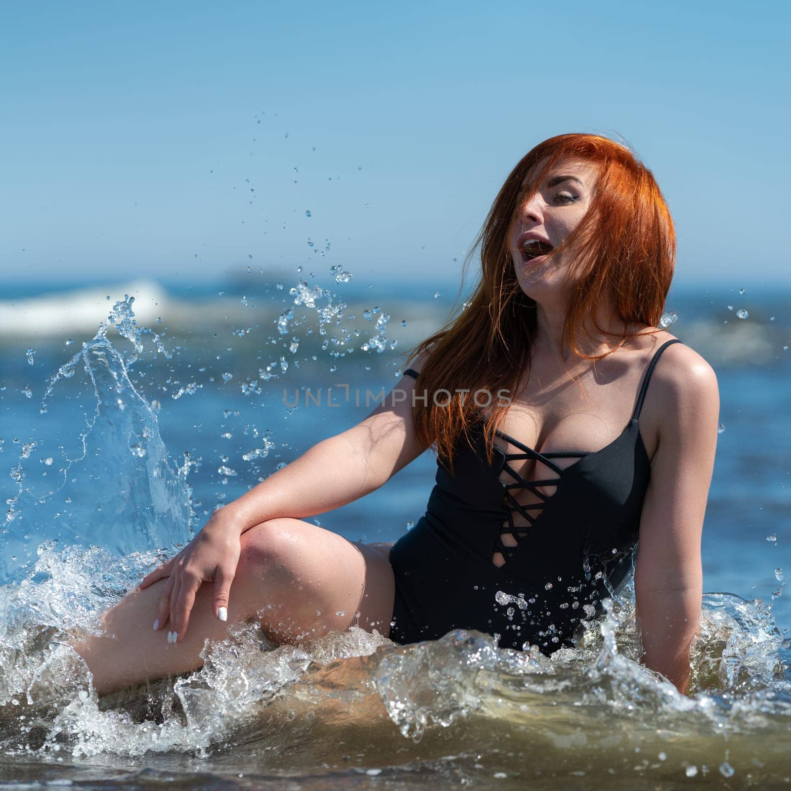 Enthusiastic playful and curvy redhead woman in black one piece swimsuit swimming and enjoying beach holiday. Her facial expression is so playful, it's impossible not to feel happy just looking at her