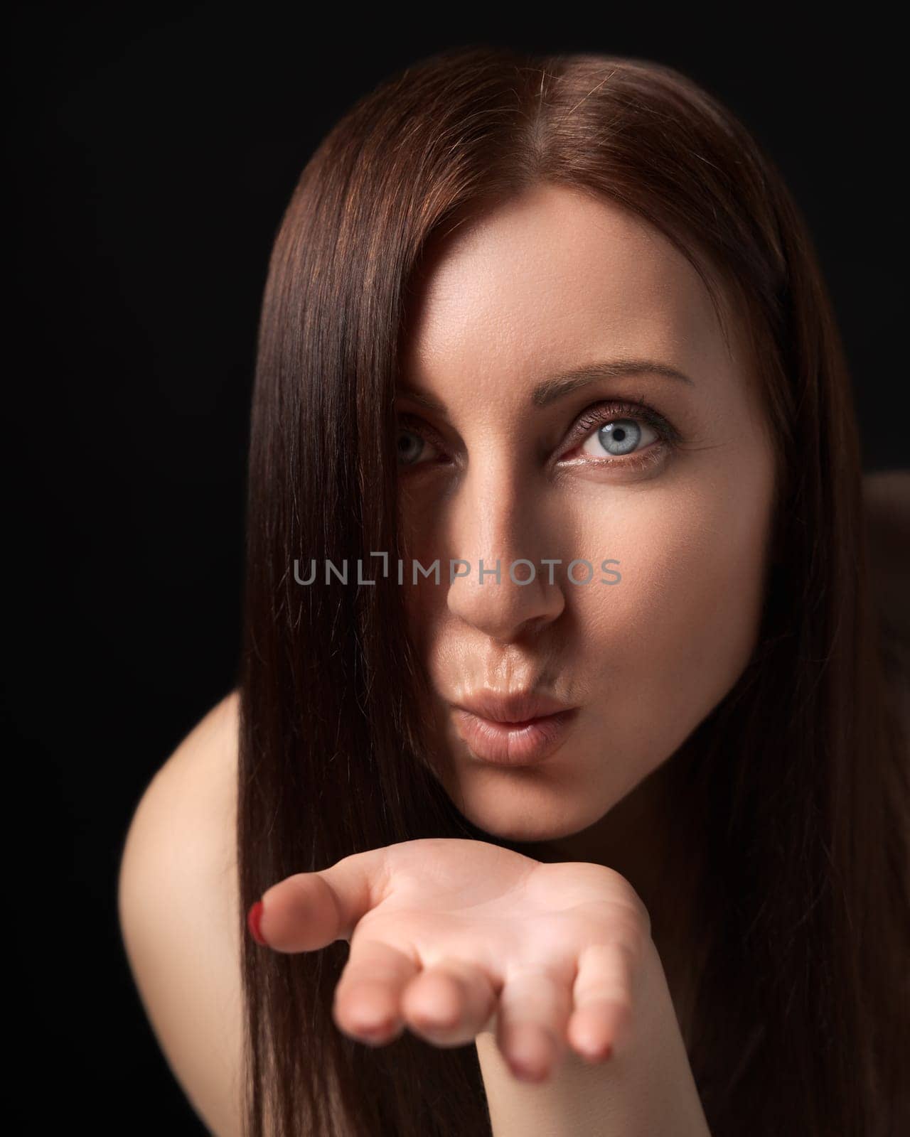 Woman blowing lips sending air kisses over palm to boyfriend, flirting - just for you. 40-year-old Caucasian ethnicity woman with long hair covering one eye showing love and looking at camera.