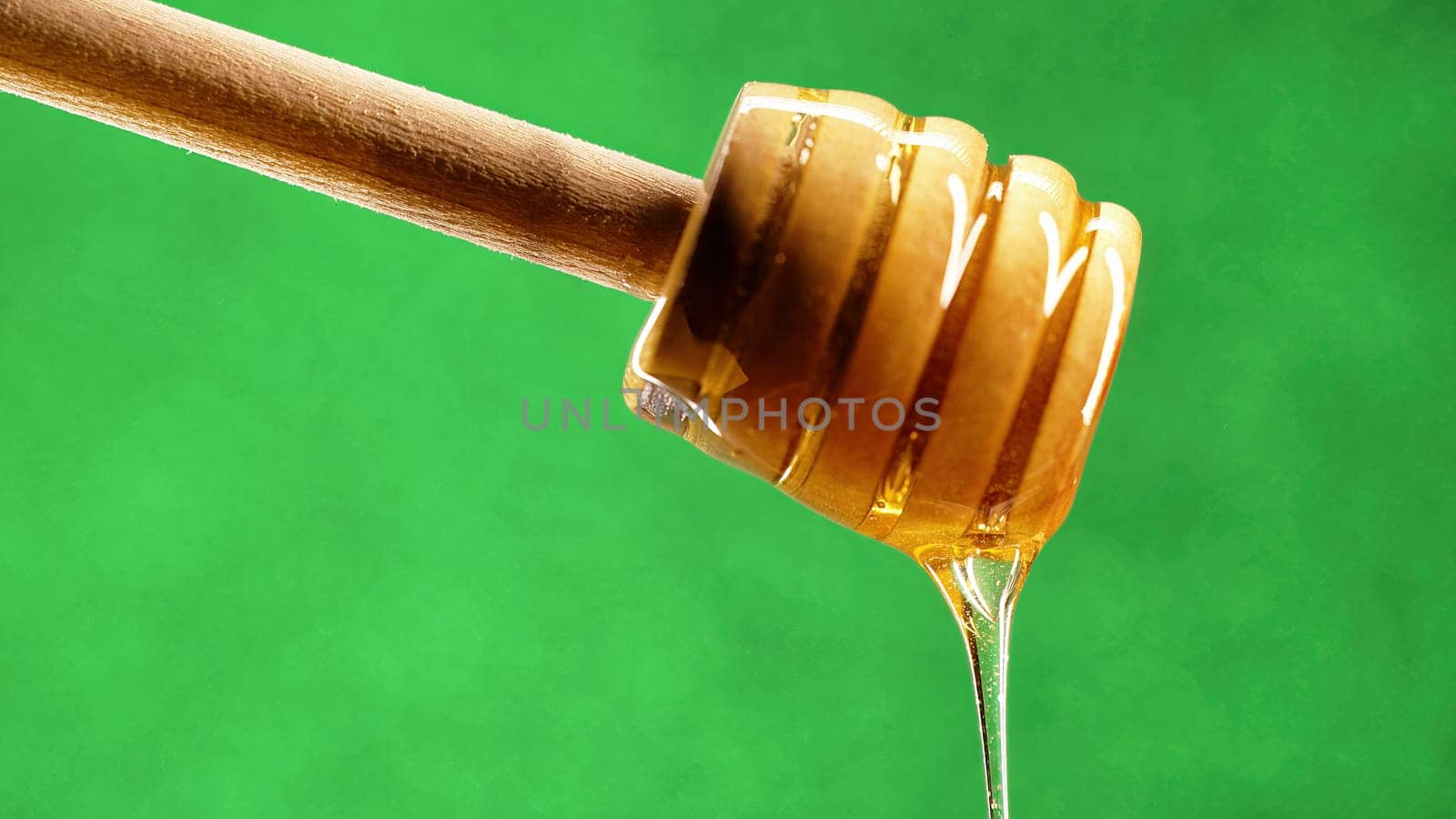 Organic honey flows from olive wood dipper stick spoon, tasty process. Apiary, beekeeping concept. Dripping, pouring sweet fluid nectar in slow motion. High quality