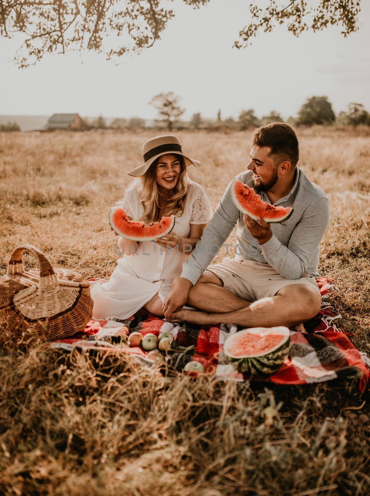 happy European caucasian family with a pregnant woman relaxing in nature picnic eating fruit red juicy watermelon laugh having fun. expectant mother in hat and dress eating watermelon in summer.