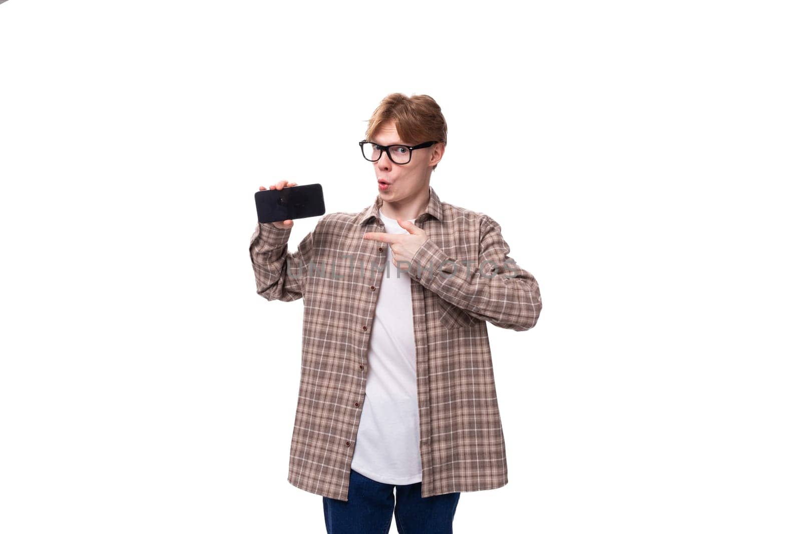 young stylish man with red hair dressed in a summer shirt shows a phone with a mockup.