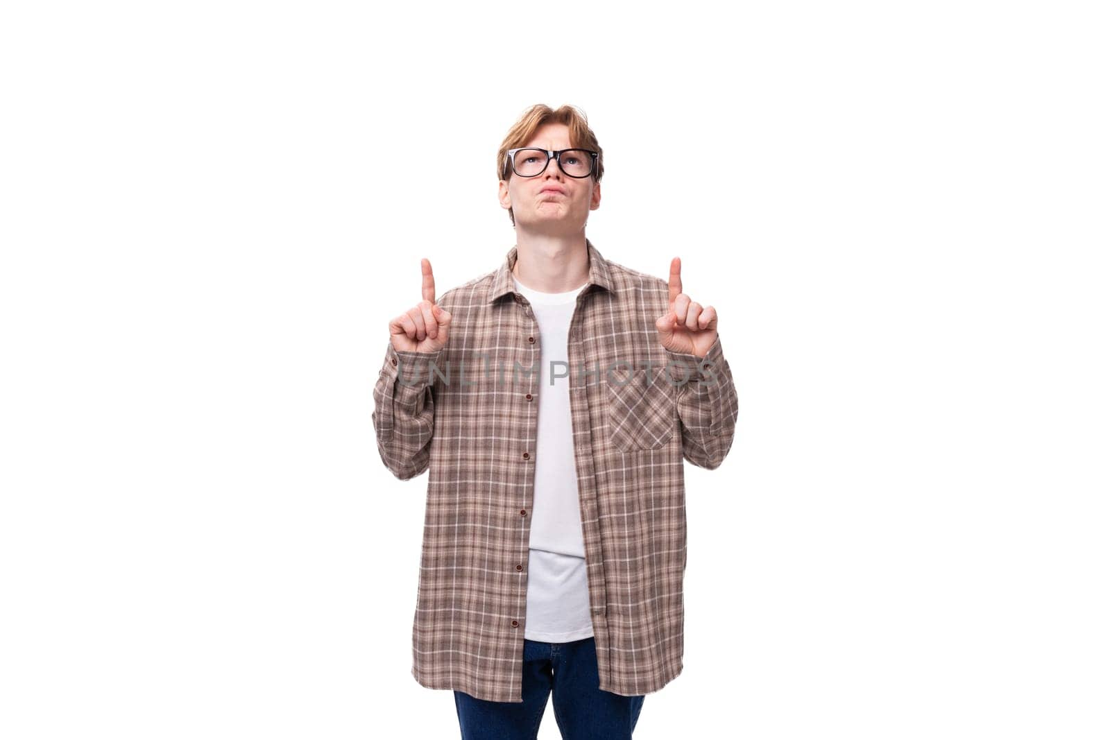 a young man with red hair dressed in a plaid shirt points with his hand to copy space by TRMK