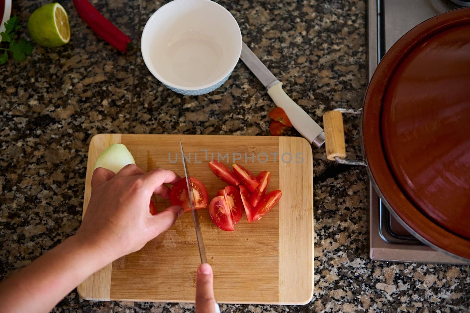 Close-up view from above of a cook chef, using kitchen knife slicing chopping cutting tomatoes on a wooden board. Food background