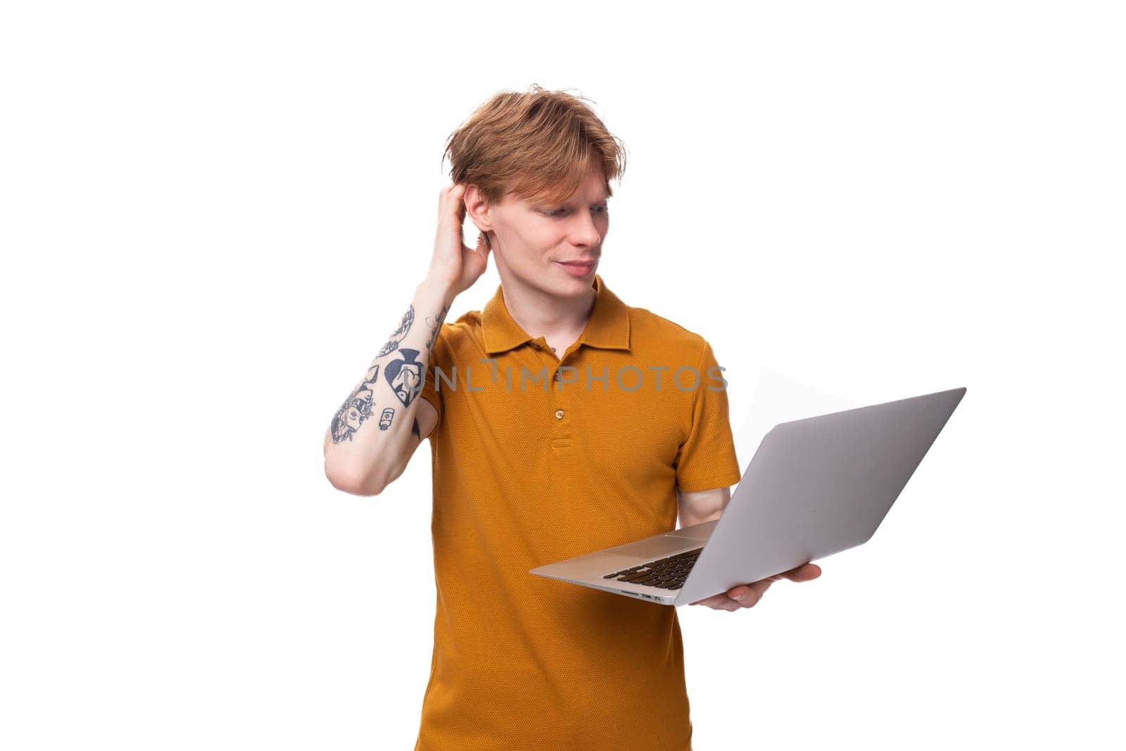 young red-haired guy in an orange t-shirt is studying using a laptop on a white background with copy space.
