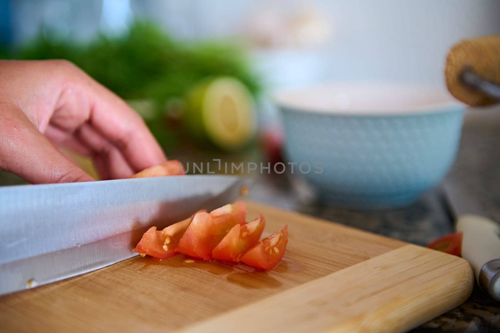 Cropped view of a chef cook slicing red juicy tomatoes on a wooden cutting board. Food background. The process of preparing a fresh healthy salad