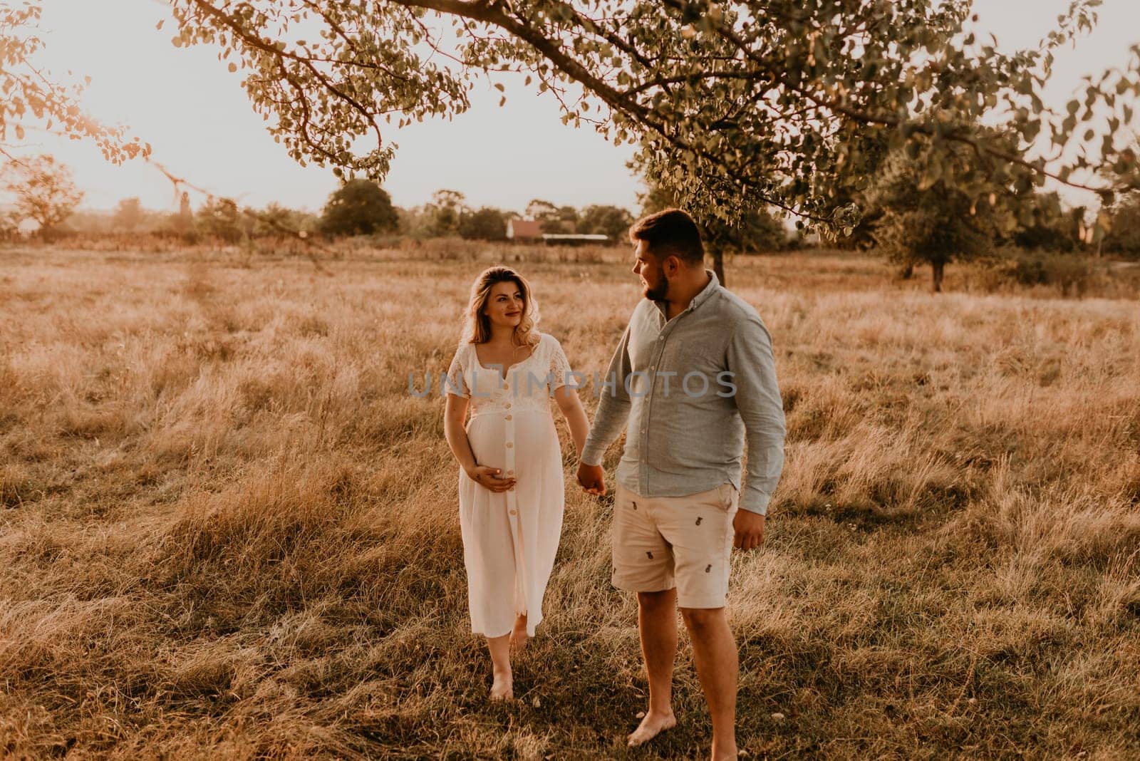 Happy family pregnant caucasian blonde woman walks with husband in meadow in summer. by AndriiDrachuk