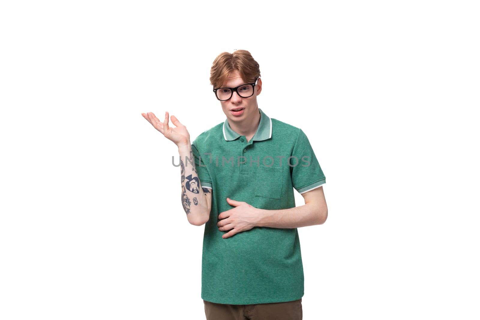 young handsome caucasian red-haired man dressed in a green t-shirt shrugs his shoulders and looks indignant by TRMK