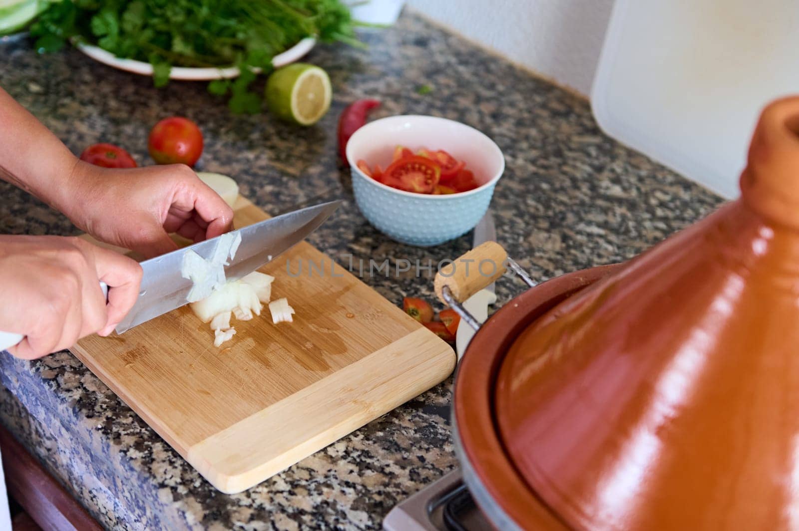 View form above. Close-up housewife's hands using a kitchen knife, chopping onion on wooden cutting board, preparing salad for dinner at home. Healthy eating concept. Food background. Culinary
