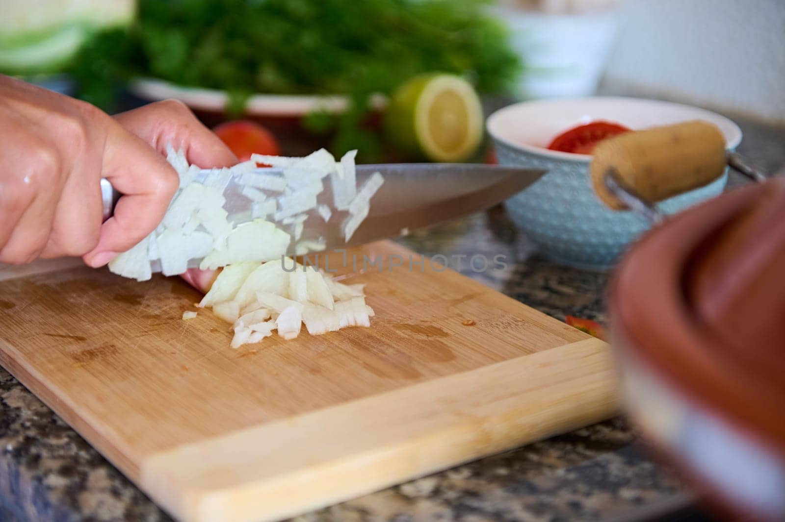 Close-up chef's hands chopping onion on wooden cutting board, preparing dinner at home. Healthy eating concept. Food background. Culinary
