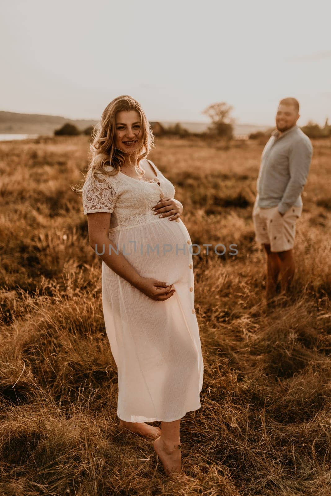 Happy family pregnant caucasian blonde woman with moles in white cotton dress walks with husband by AndriiDrachuk