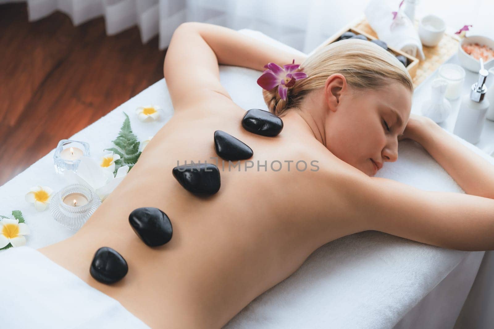 Hot stone massage at spa salon in luxury resort with day light serenity ambient, blissful woman customer enjoying spa basalt stone massage glide over body with soothing warmth. Quiescent