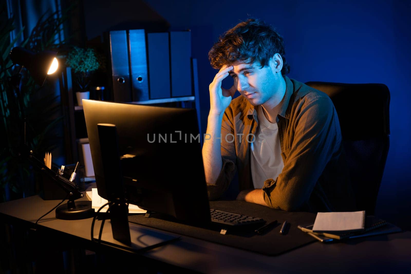 Stressful creative manager searching design thinking with new presentation while waiting email sending back on laptop screen at home office in casual shirt at neon light room at night time. Gusher.