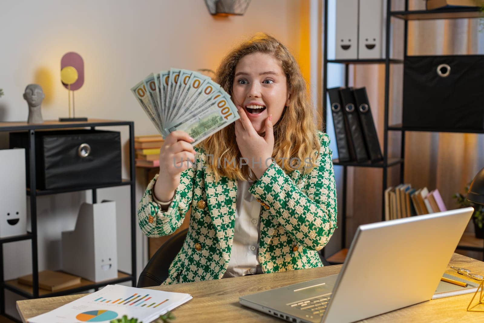 Rich Caucasian businesswoman girl earnings big profit success win lottery wasting money profit shopping more tips. Happy young blond freelancer woman manager with laptop at home office desk.