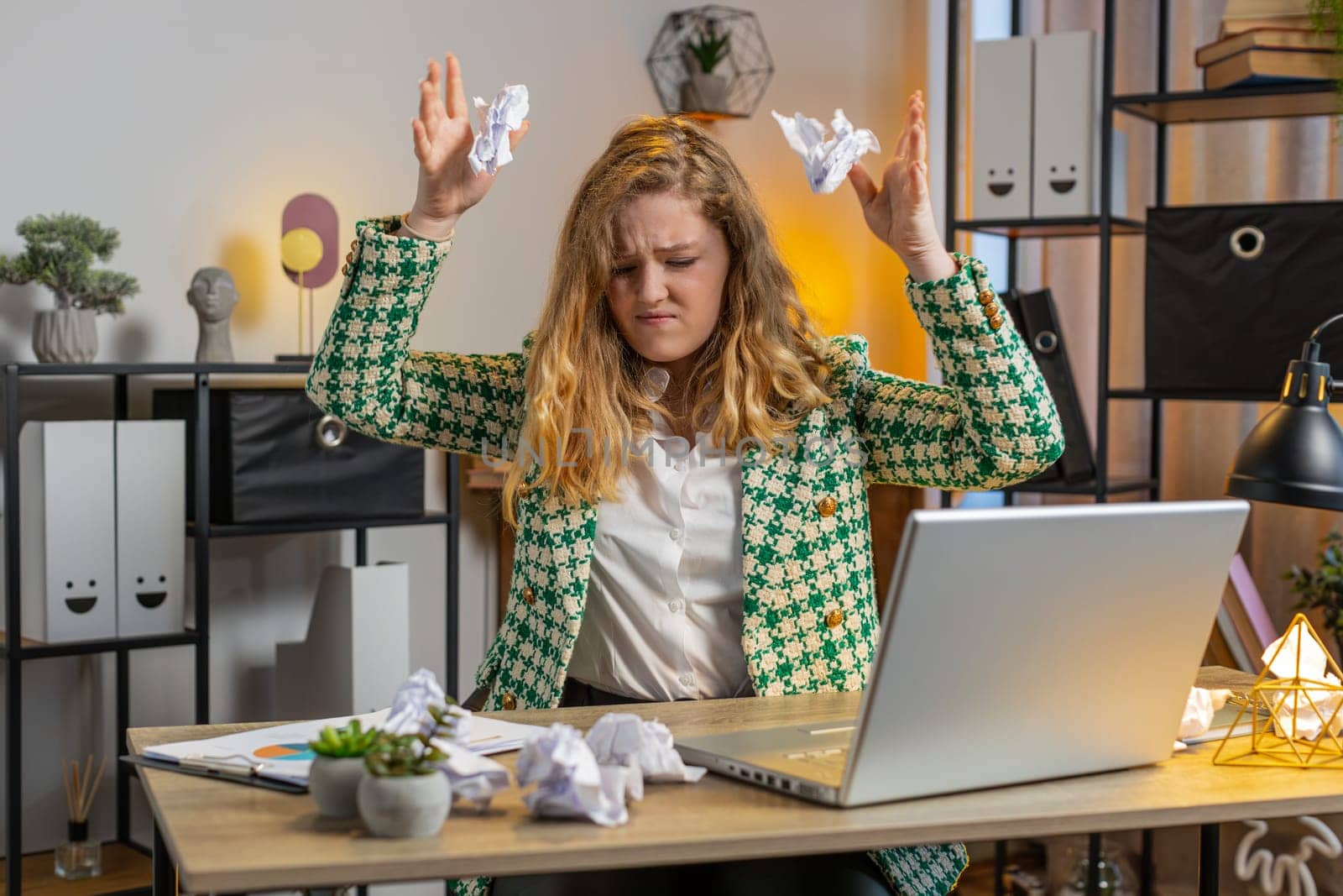 Angry furious Caucasian businesswoman throwing crumpled paper nervous breakdown at work stress management mental distress problems losing temper reaction on failure. Girl sits at home office at desk.