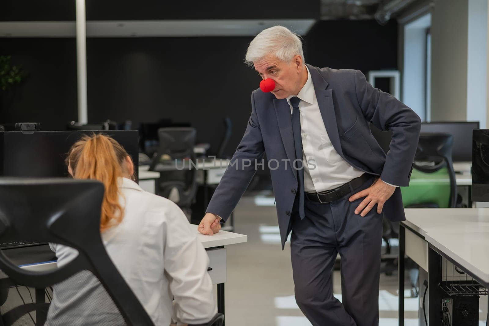 Elderly Caucasian man wearing a clown nose swears at his subordinate in the office