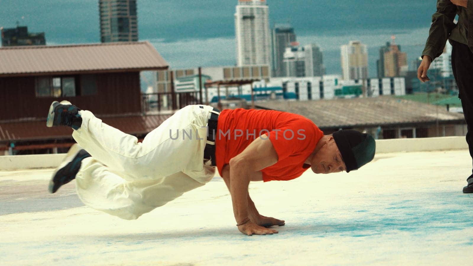 Caucasian hipster doing freeze pose in B-boy performance at roof top of high building. Young professional man break dancing at rooftop with city or urban view background. Outdoor sport 2024. Endeavor.