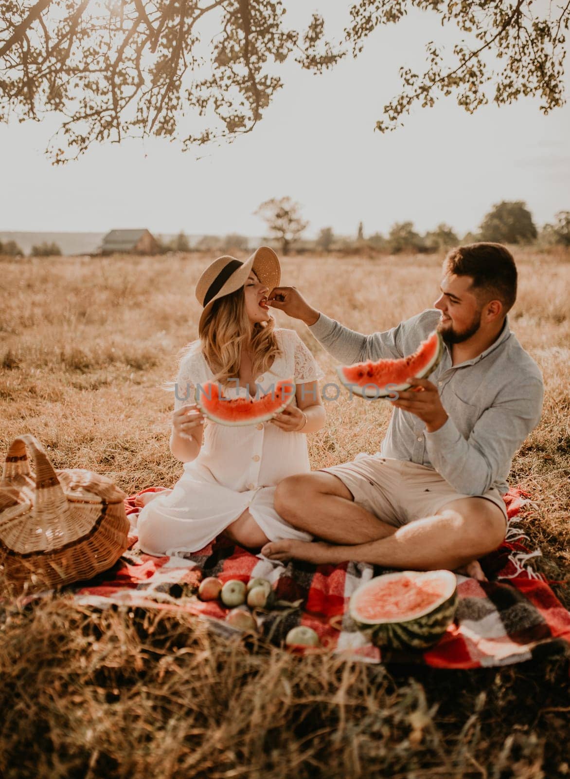 happy European caucasian family with a pregnant woman relaxing in nature picnic eating fruit red juicy watermelon laugh having fun. expectant mother in hat and dress eating watermelon in summer.