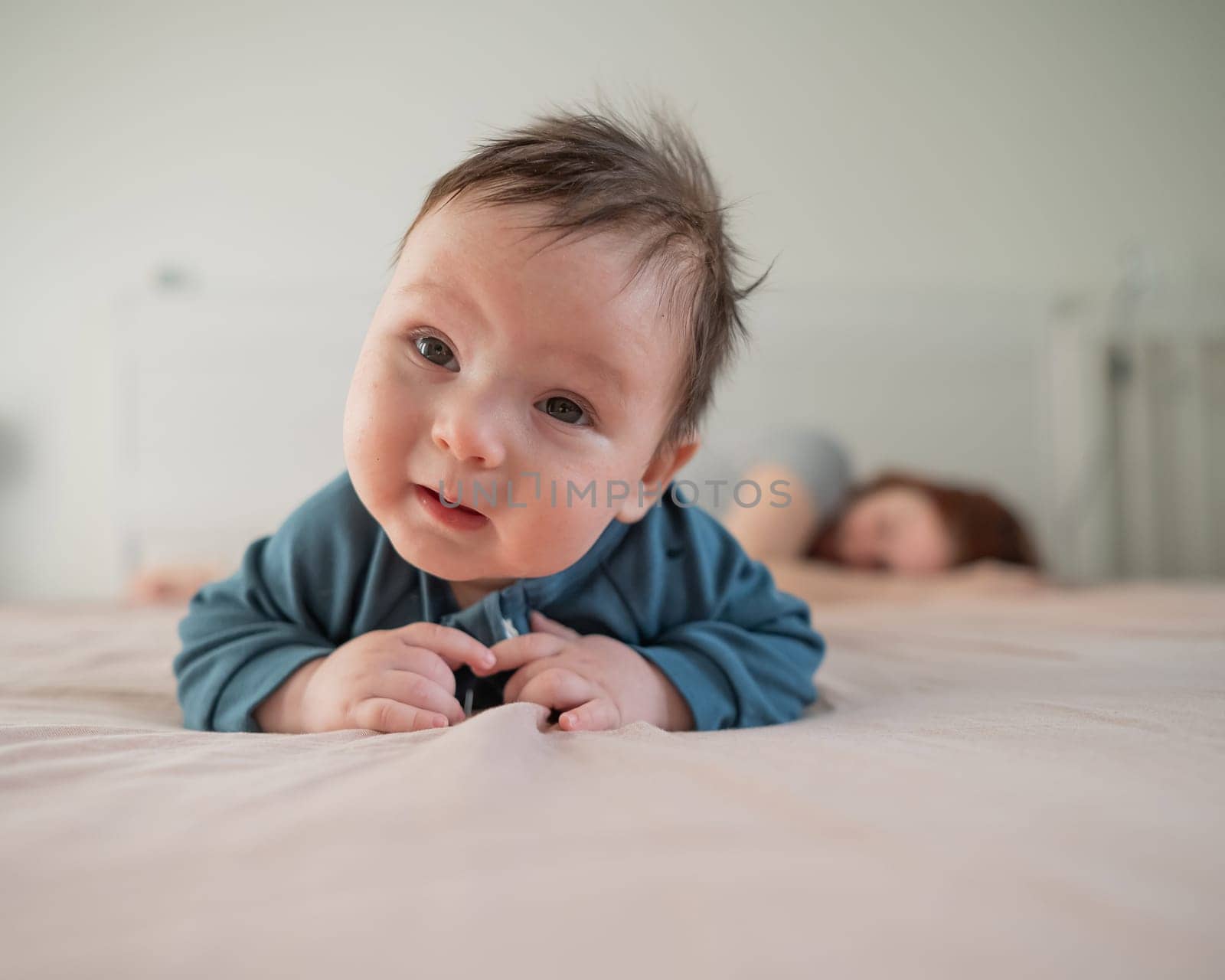 A three-month-old boy lies on his stomach on the bed and his mother sleeps behind him. Postpartum depression. by mrwed54