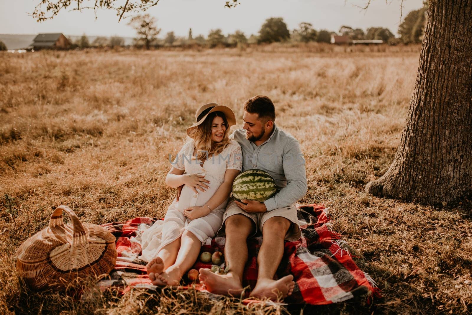 caucasian family with a pregnant woman relaxing in nature picnic eating watermelon laugh having fun by AndriiDrachuk