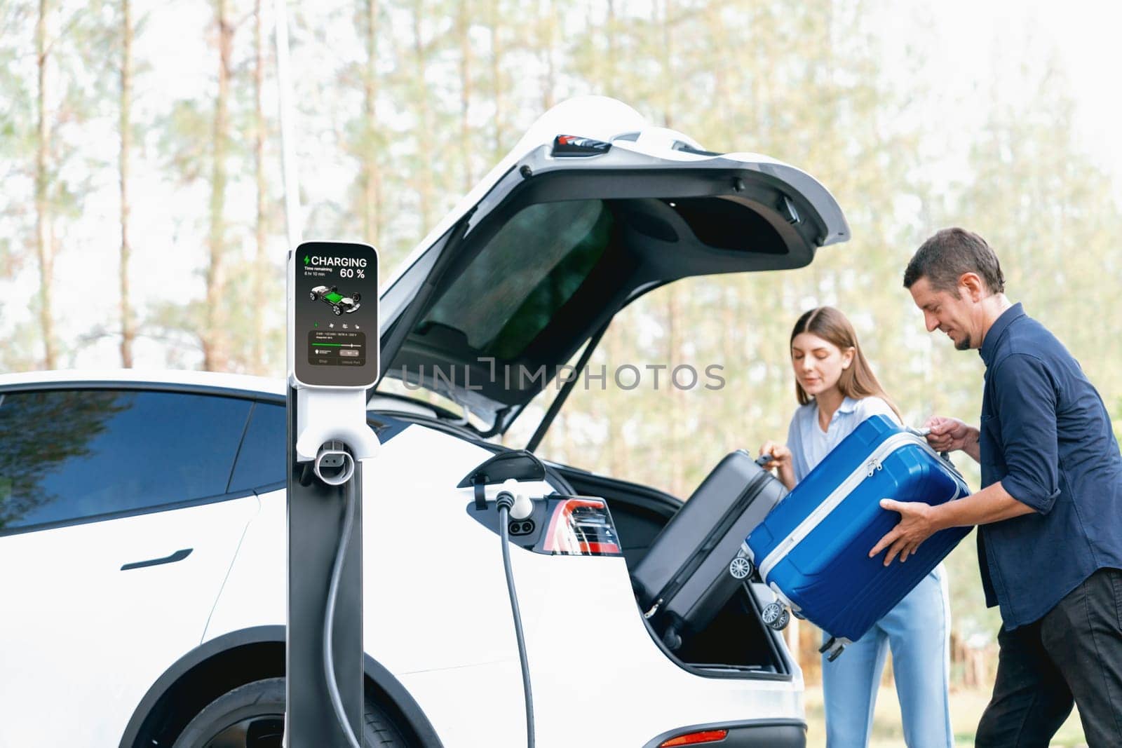 Lovely young couple recharging battery for electric car in autumn. Exalt by biancoblue