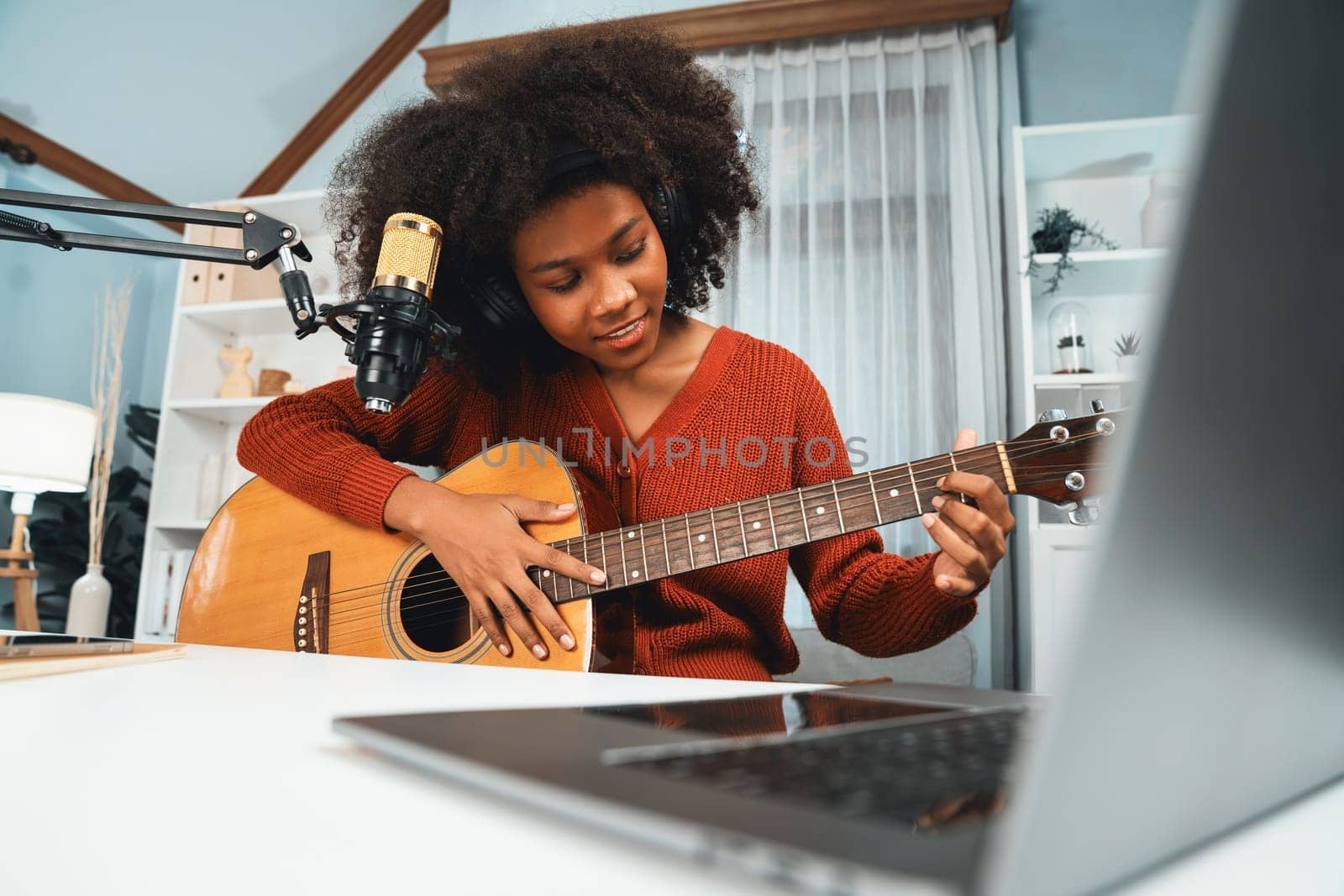 Host channel in musician of young African American playing guitar along with singing, broadcasting on laptop in studio. Decoration of equipment of headsets and recording microphone. Tastemaker.