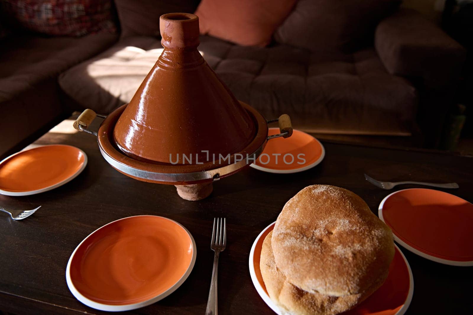 Traditional Moroccan tasty meal cooked in tagine clay pot with freshly baked bread on the table at home. Cultures, traditions and national cuisine of Morocco