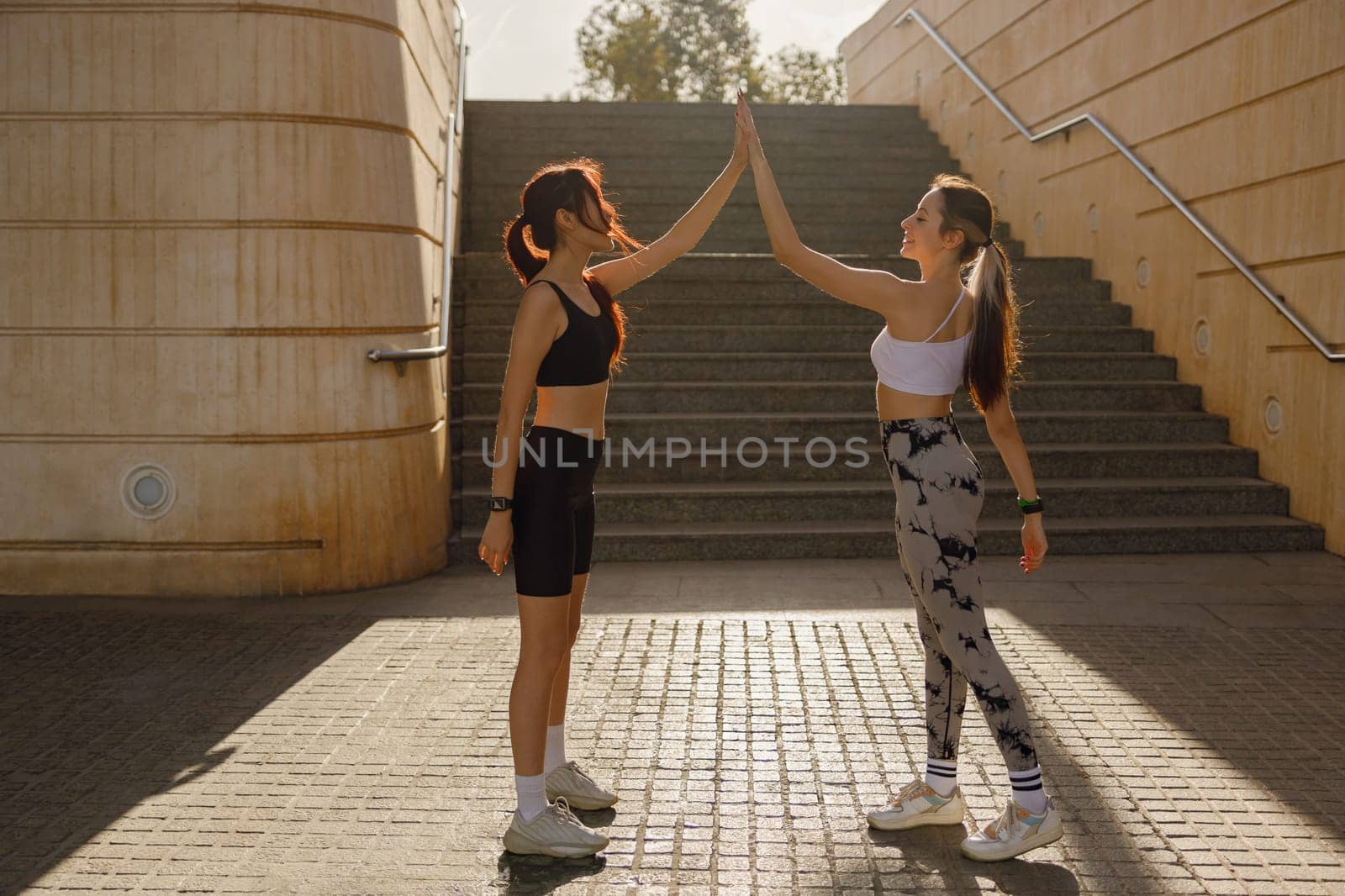 Happy female friends doing gesture of sport shake hand after exercising outside by Yaroslav_astakhov