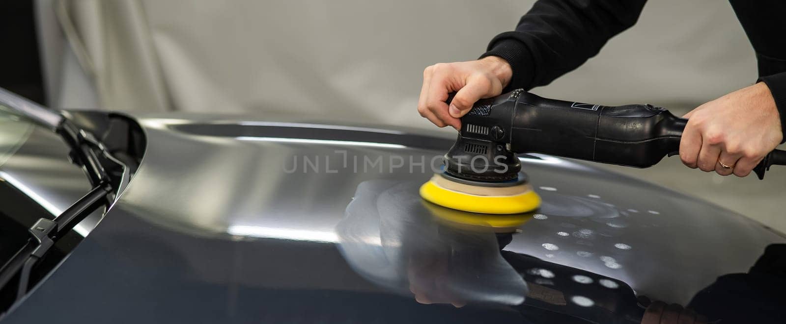 A mechanic polishes the surface of the hood of a gray car. by mrwed54