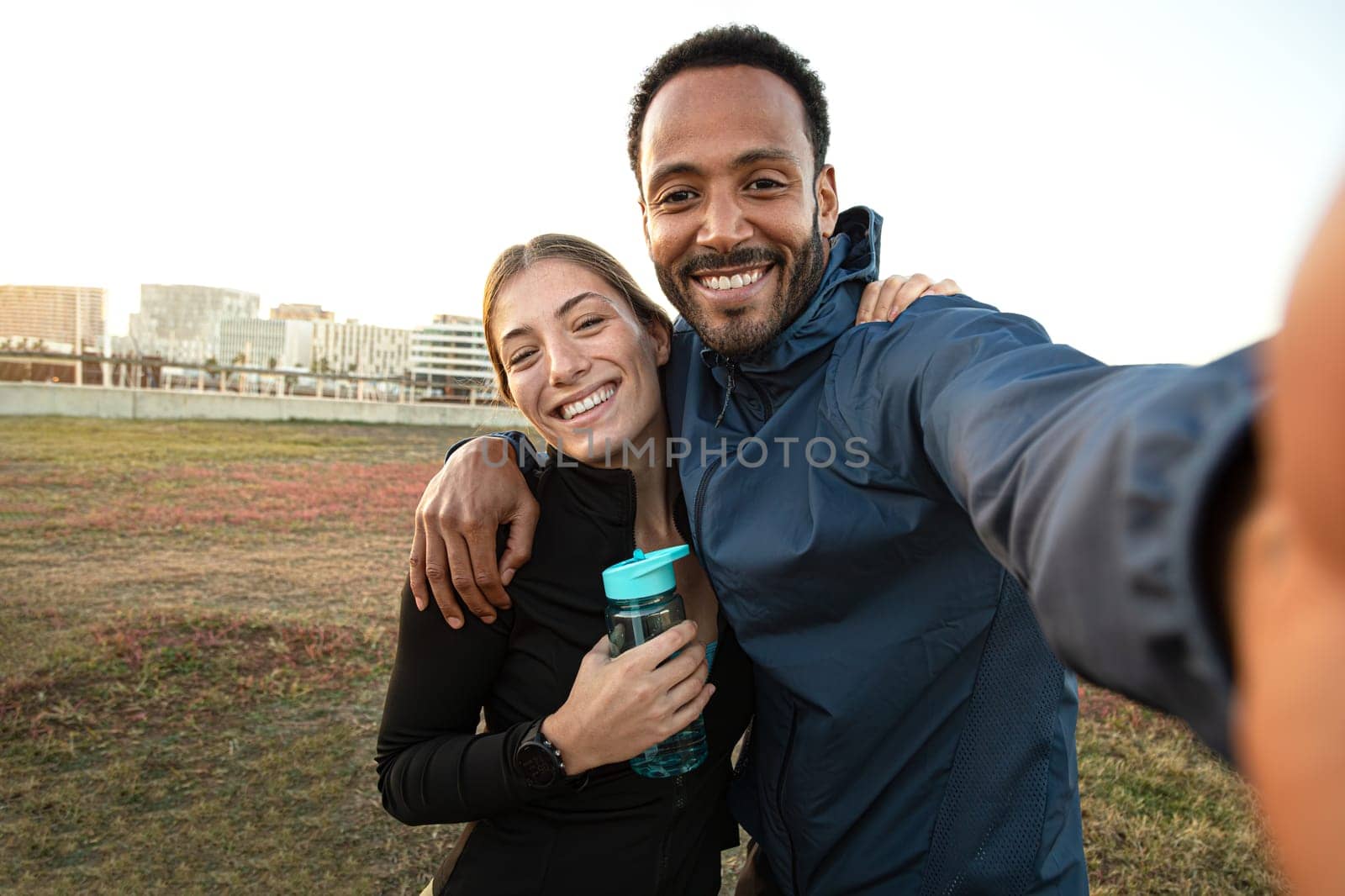 Multiracial couple taking selfie after workout outdoors. Sporty couple taking self portrait after running in the park. by Hoverstock